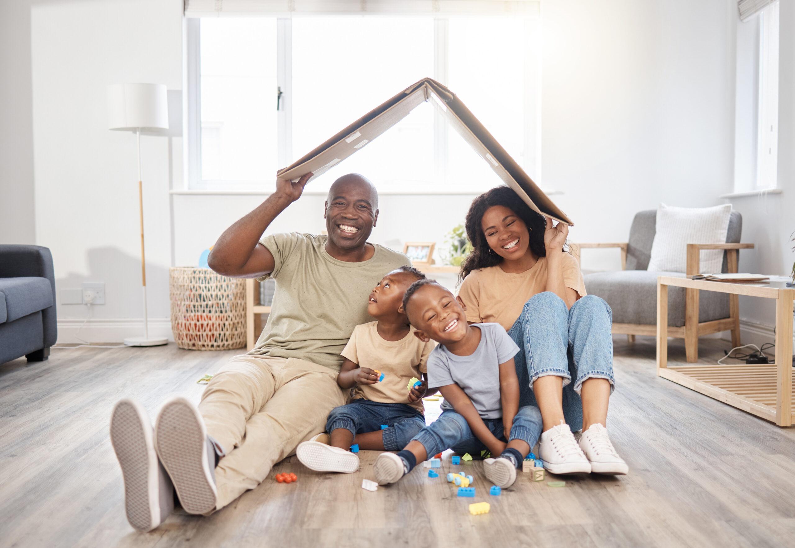 A smiling family sitting together under a cardboard roof in their living room